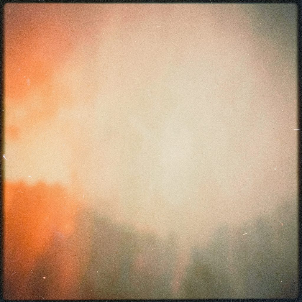 Analog film photograph of a wide border skyline at dusk, pale blues and dusty oranges with soft grain