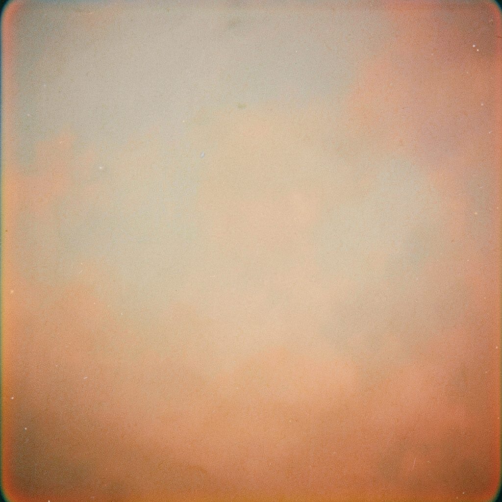 Wide analog film photograph of a northern Mexican border city, soft warm sunset light filtering through dust, distant rooftops and industrial structures in muted earth tones, visible film grain